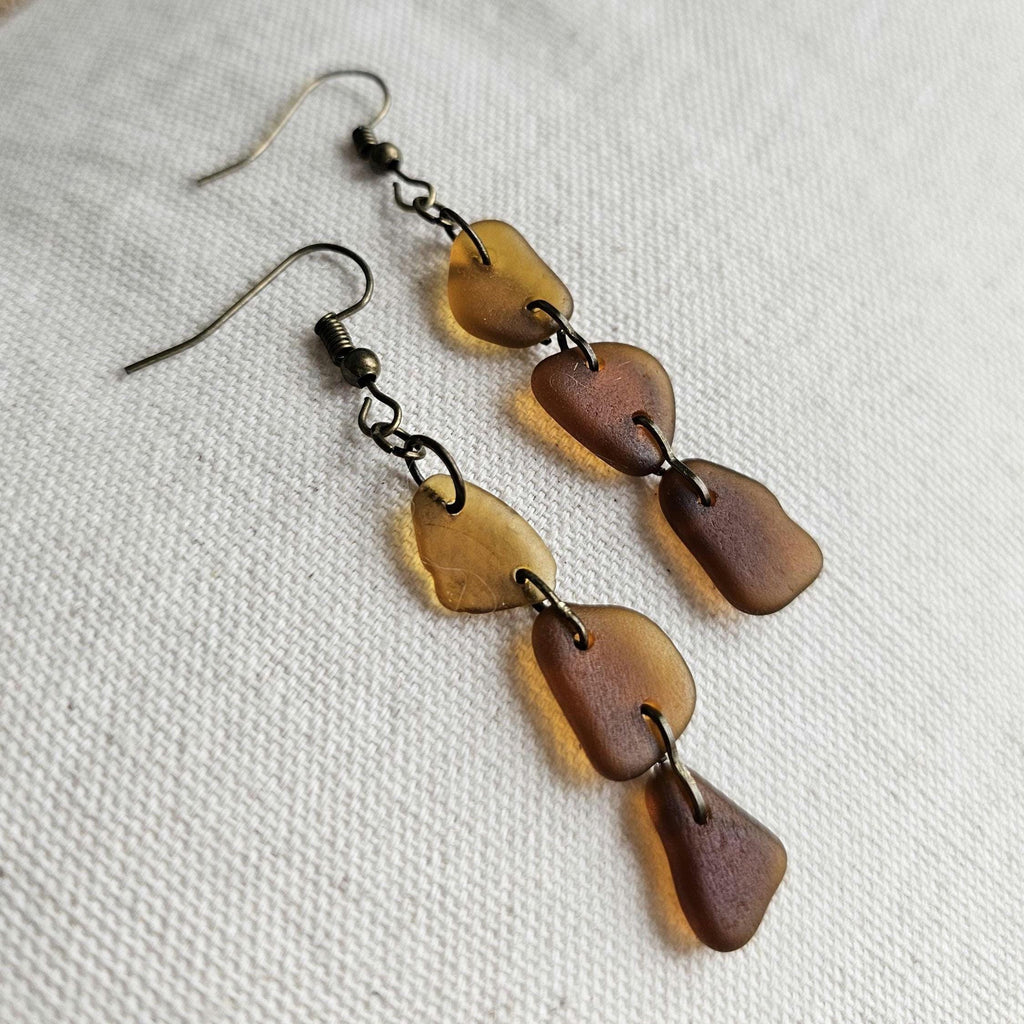 Pair of earrings with brown and gold disc shapes on a white fabric background