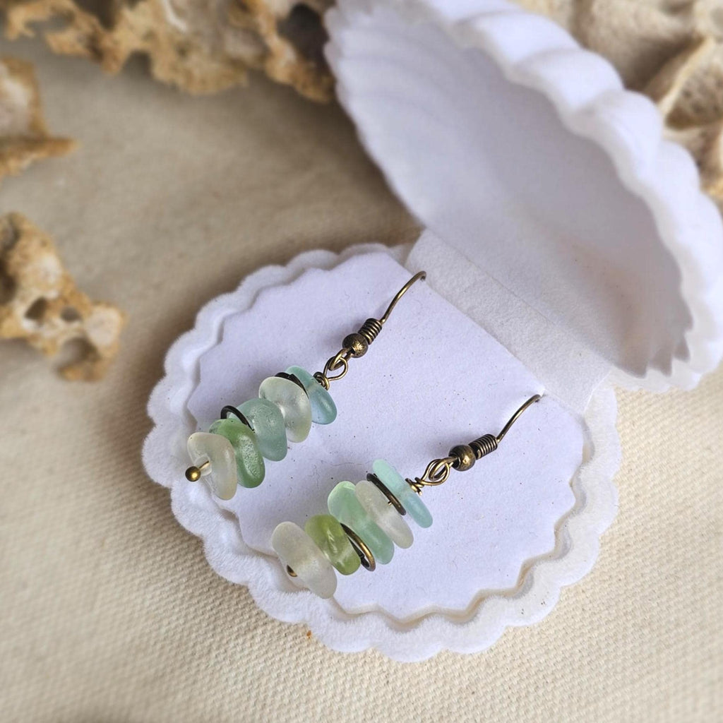 Pair of sea glass earrings with green, aqua and clear sea glass on a textured surface