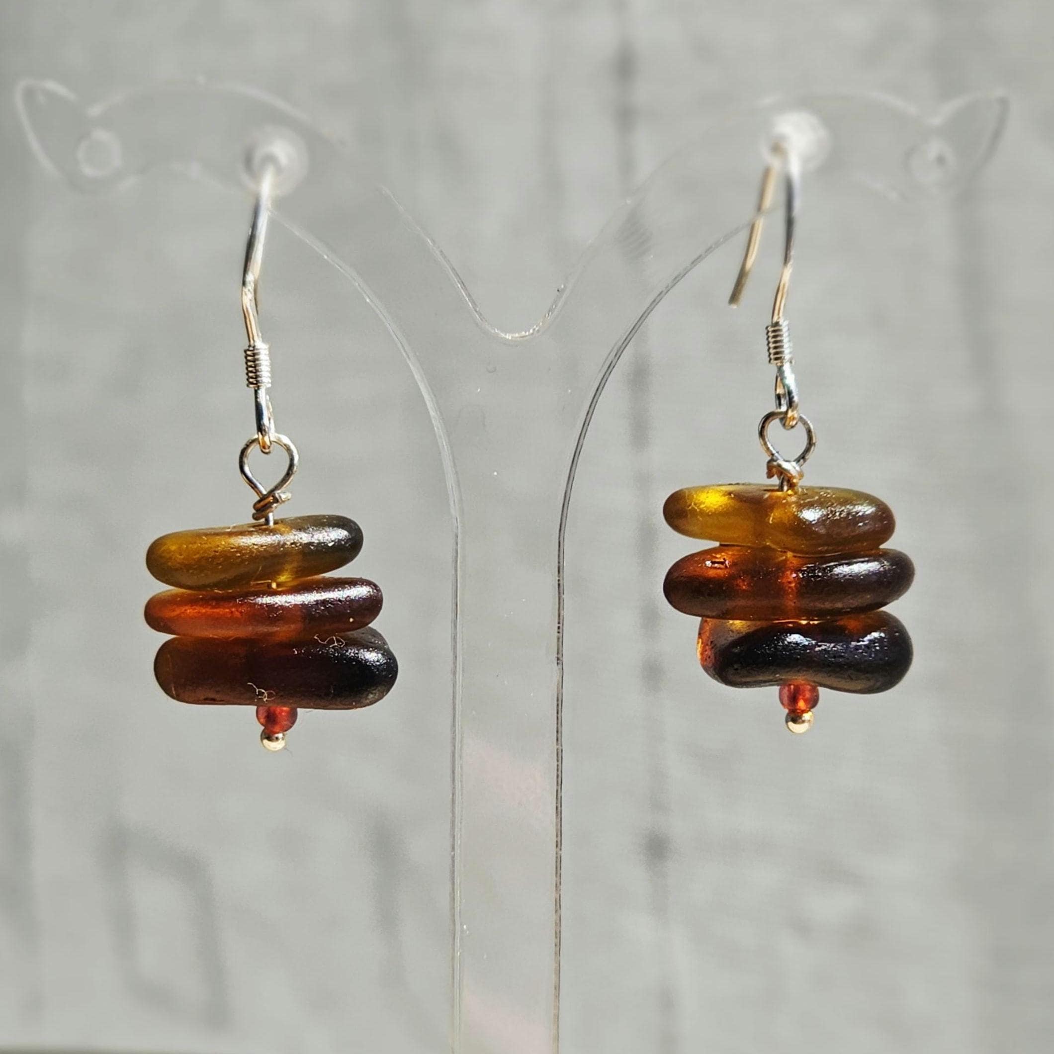 Pair of multicolored sea glass earrings on a clear stand with a gray background