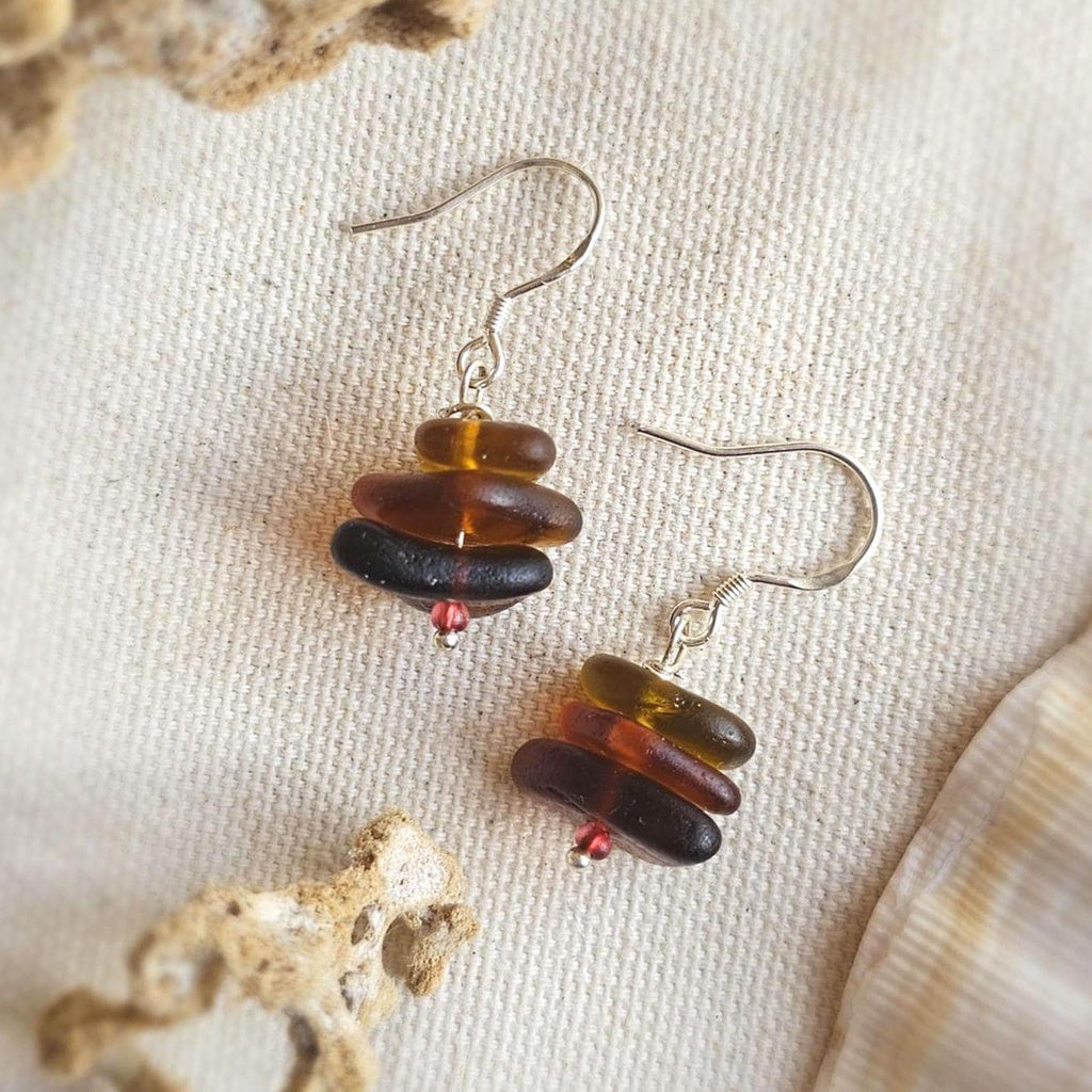 Pair of earrings with stacked amber-colored sea glass on a textured beige background