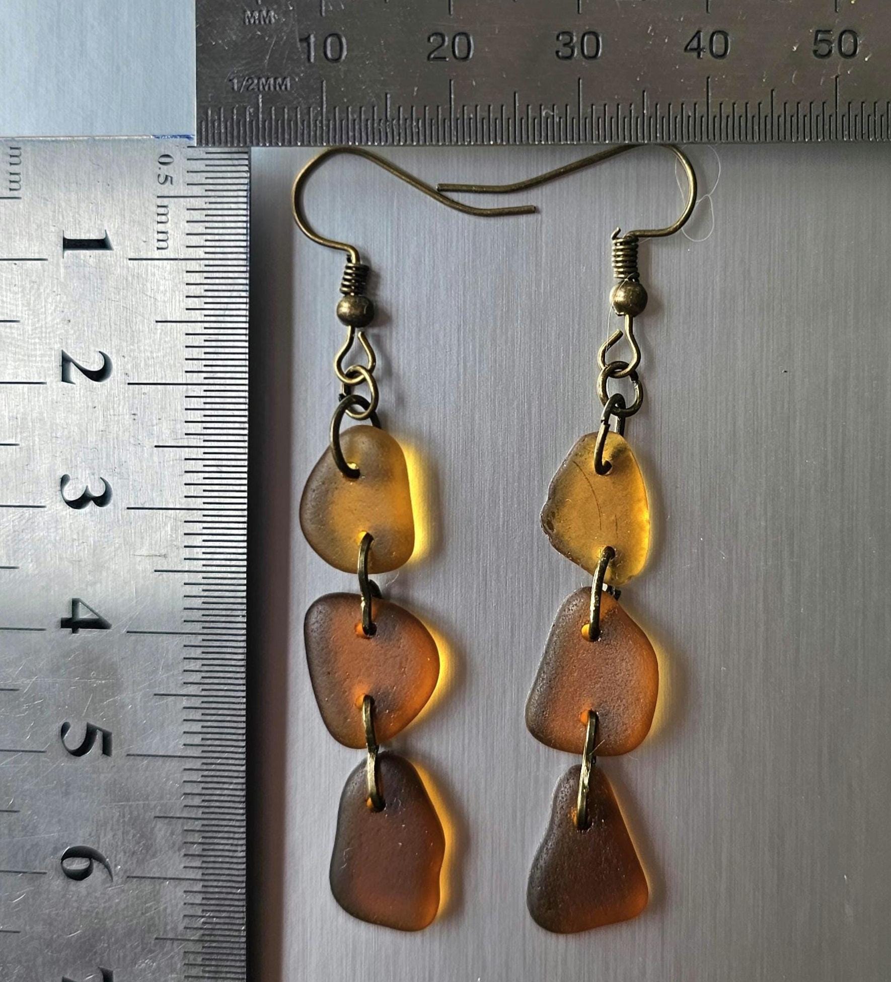 Pair of amber-colored earrings with gold hooks on a gray surface with a ruler for scale.