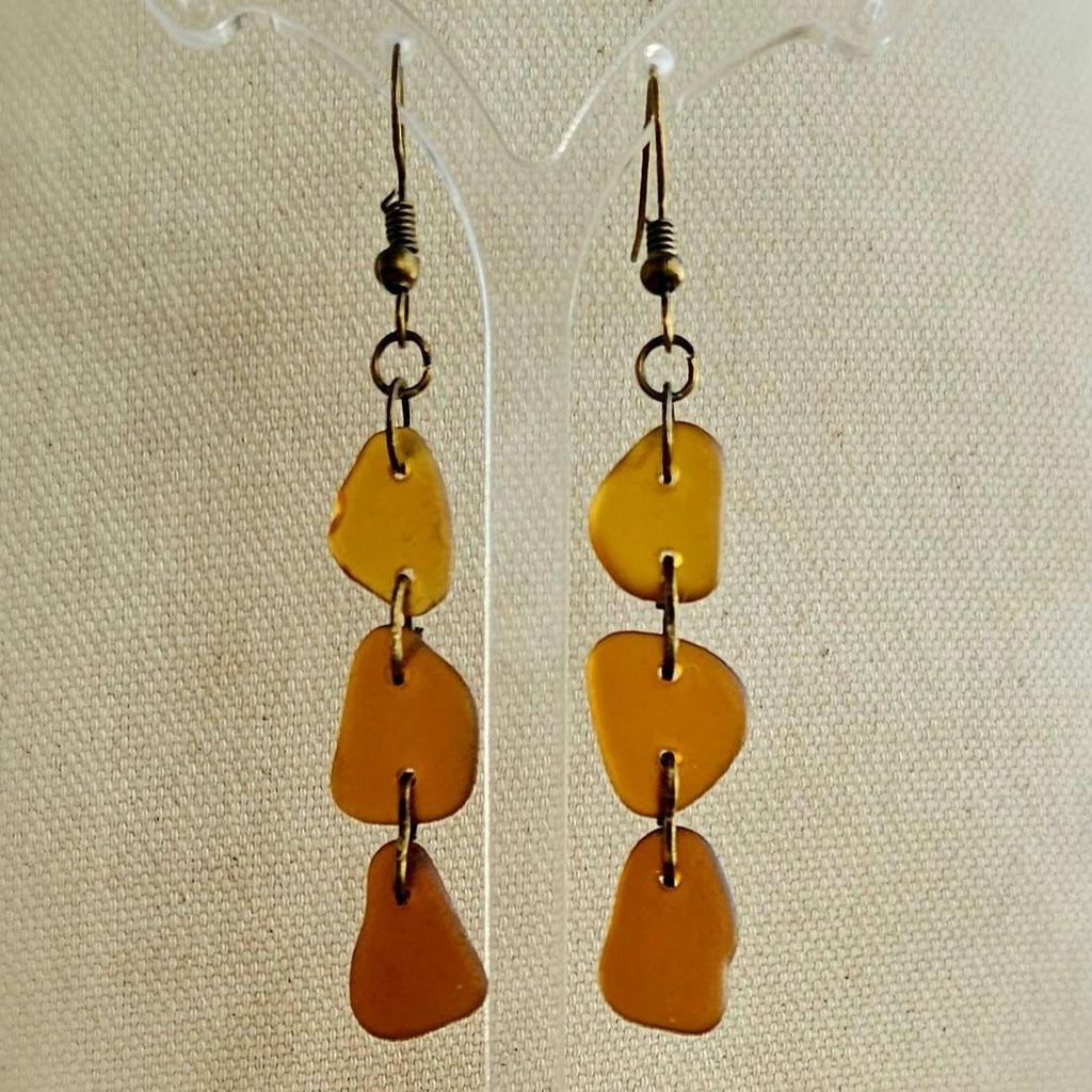 Pair of amber-colored drop earrings on a beige fabric background