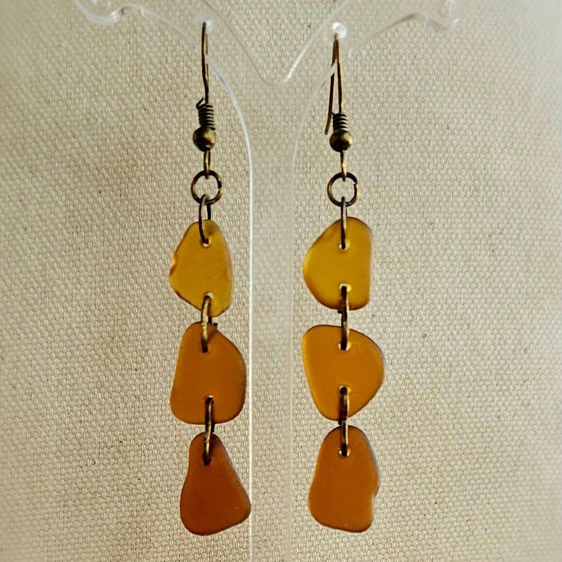 Pair of amber-colored drop earrings on a beige fabric background