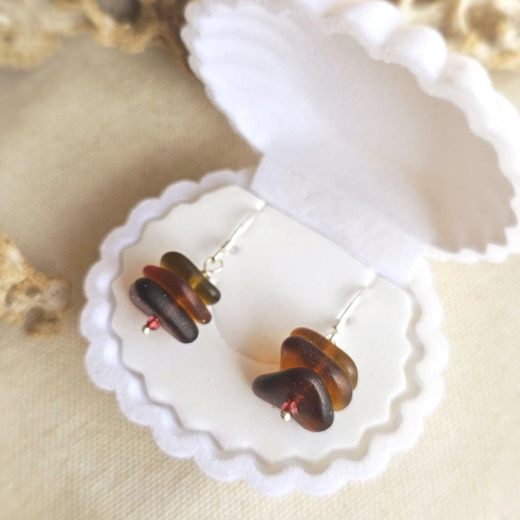 Pair of earrings with brown and amber sea glass in a white jewelry box on a beige background
