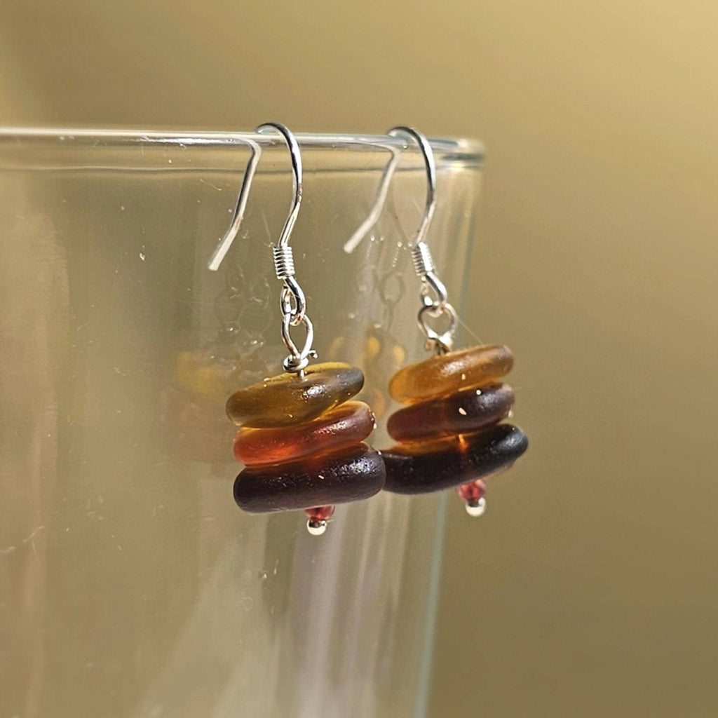 Stacked sea glass bead earrings on a clear stand against a beige background