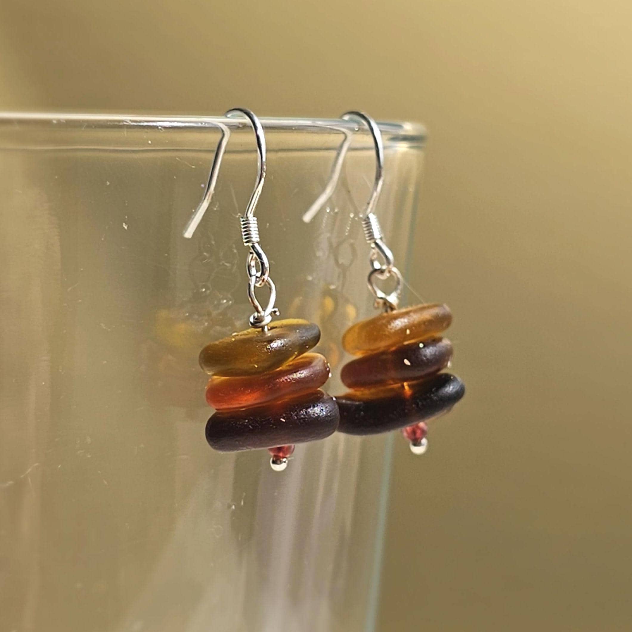 Stacked sea glass bead earrings on a clear stand against a beige background